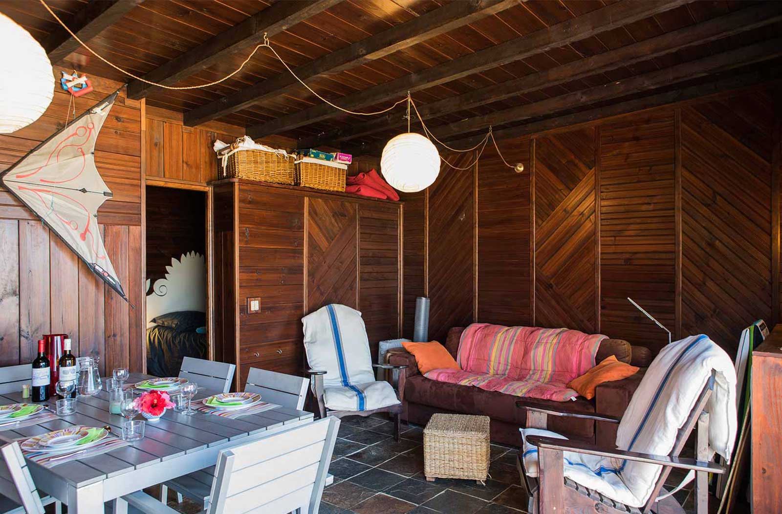 Photo d'un salon avec coin repas, les murs sont en bois, il y une table avec chaises et un canapé.