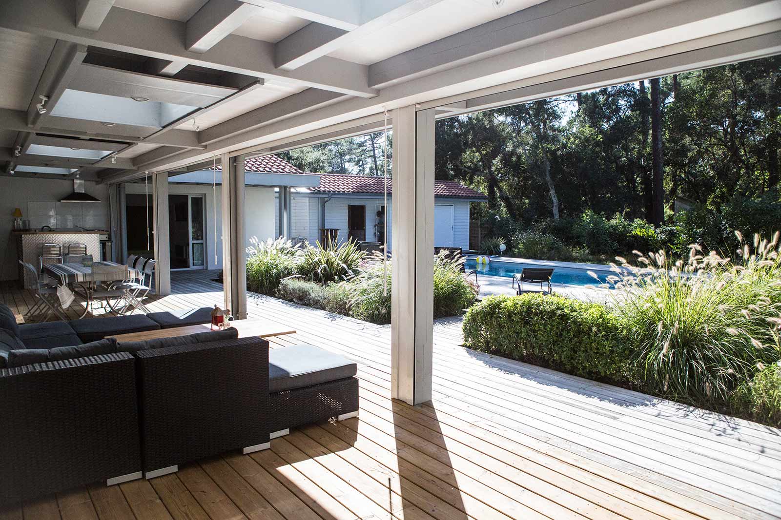 Photo d'une terrasse en bois avec meubles de jardin gris donnant sur le jardin avec piscine et transats.