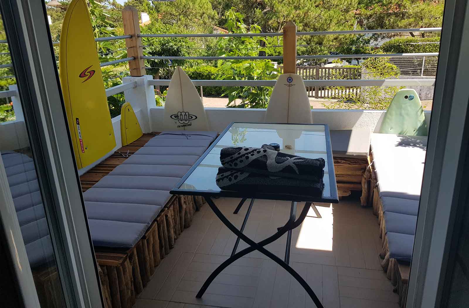 Photo du balcon terrasse avec bancs en bois et une table, des morceaux de planches de surf servent à la décoration.