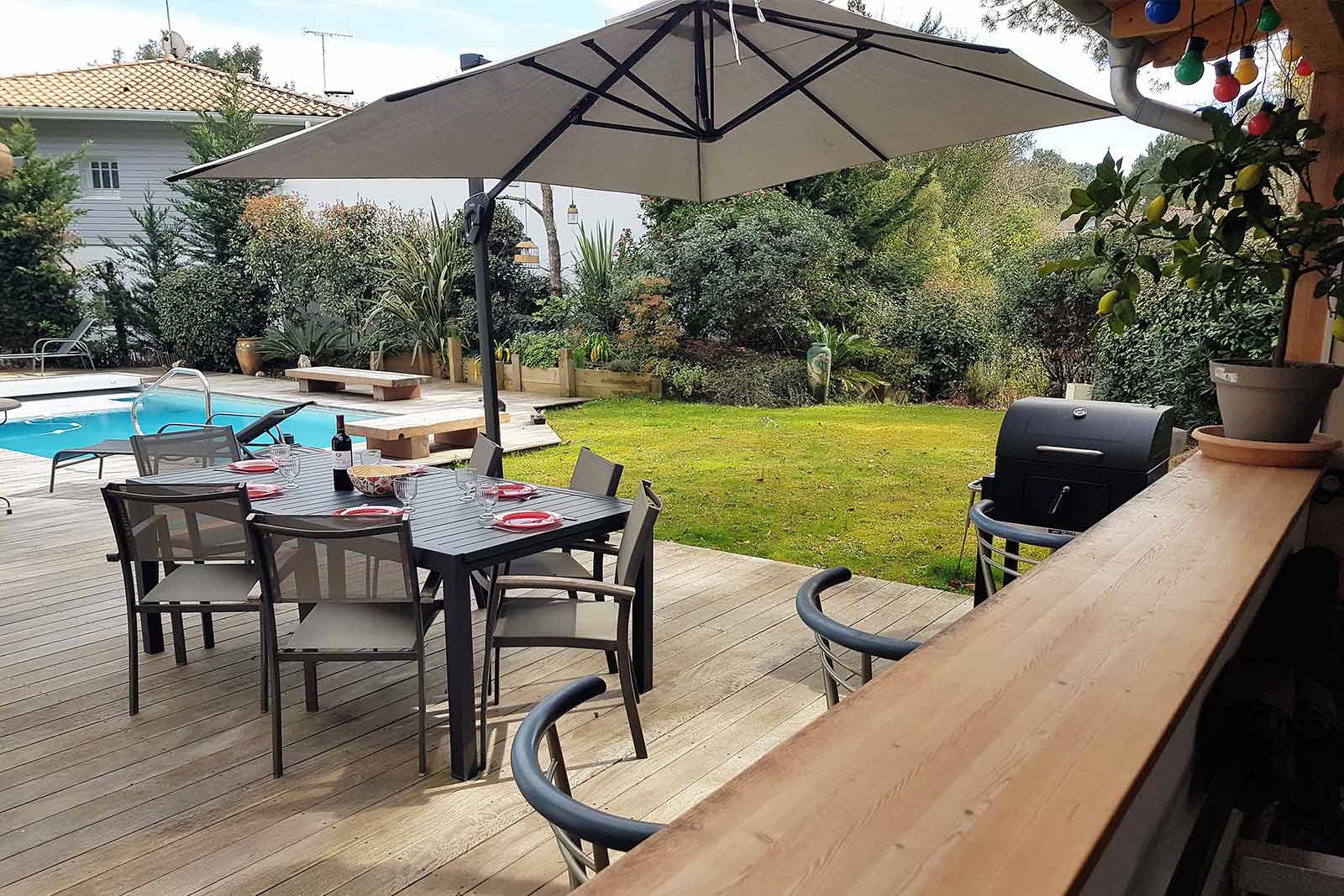 Photo de la terrasse du cabanon, avec vue sur l'océan, table, parasol et transats posés sur le sable.