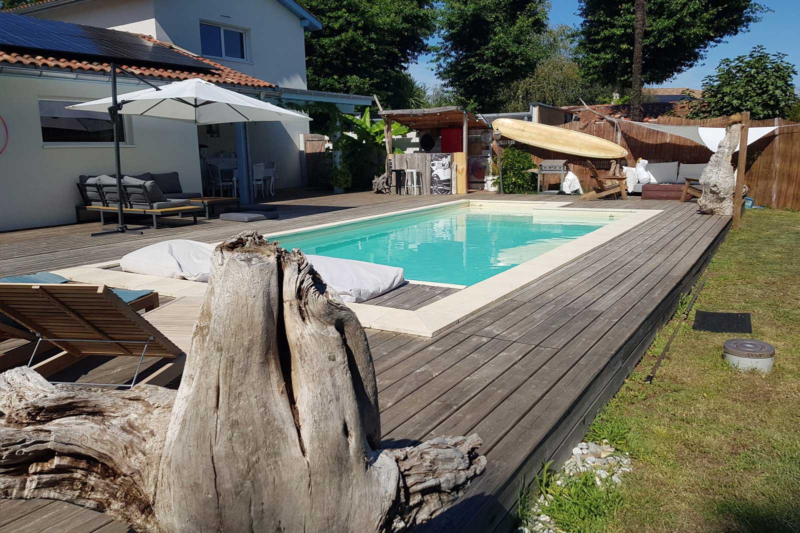 Photo de la terrasse du cabanon, avec vue sur l'océan, table, parasol et transats posés sur le sable.